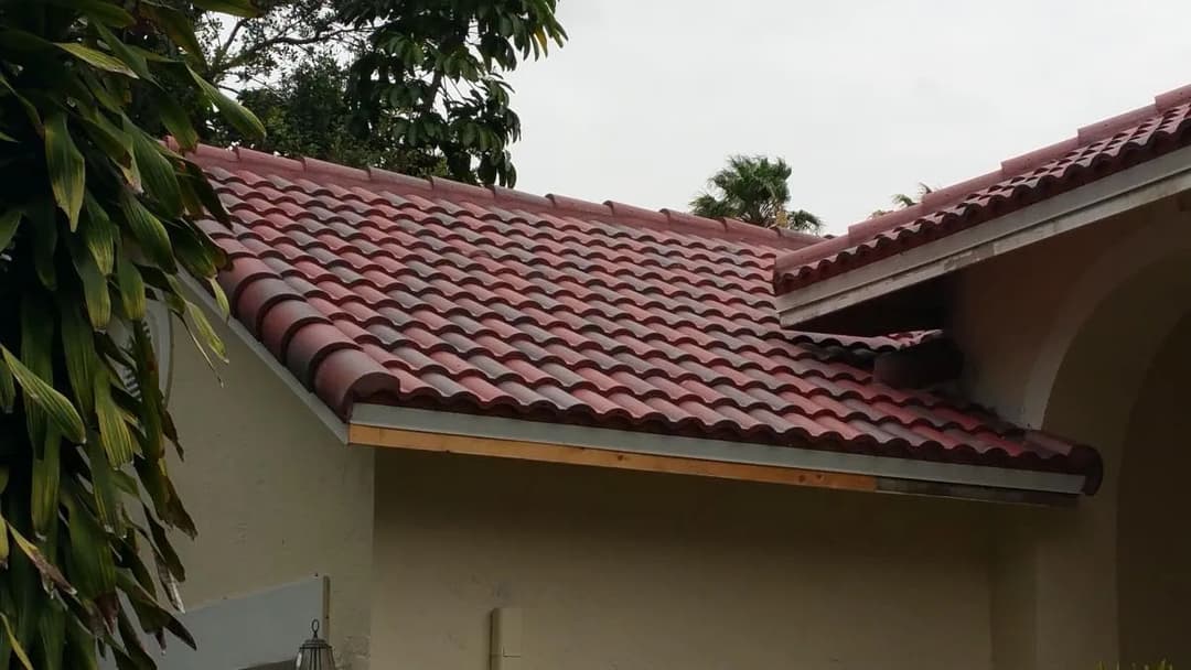 Red tiled roof on a residential building, surrounded by greenery and palm trees.