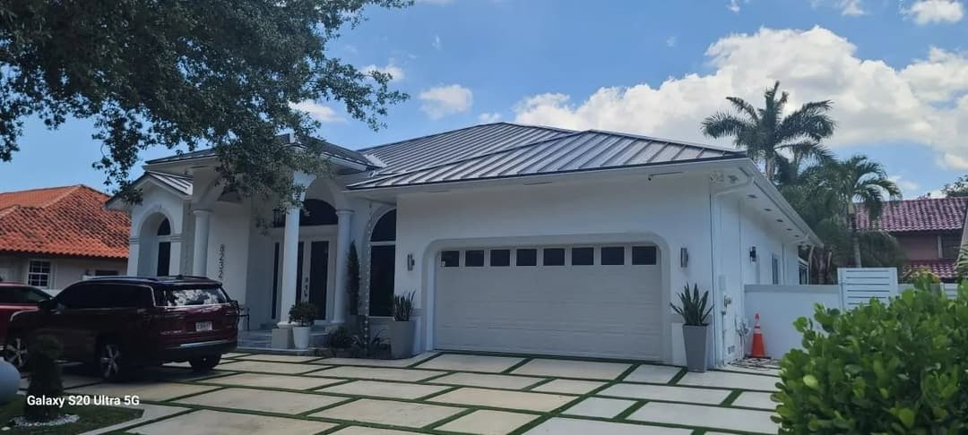 Modern white house with a metal roof and landscaped driveway under a blue sky.