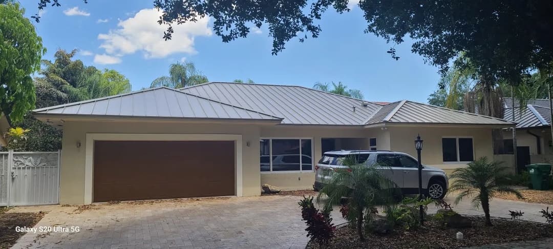 Modern single-story home with a metal roof, parked car, and palm landscaping.