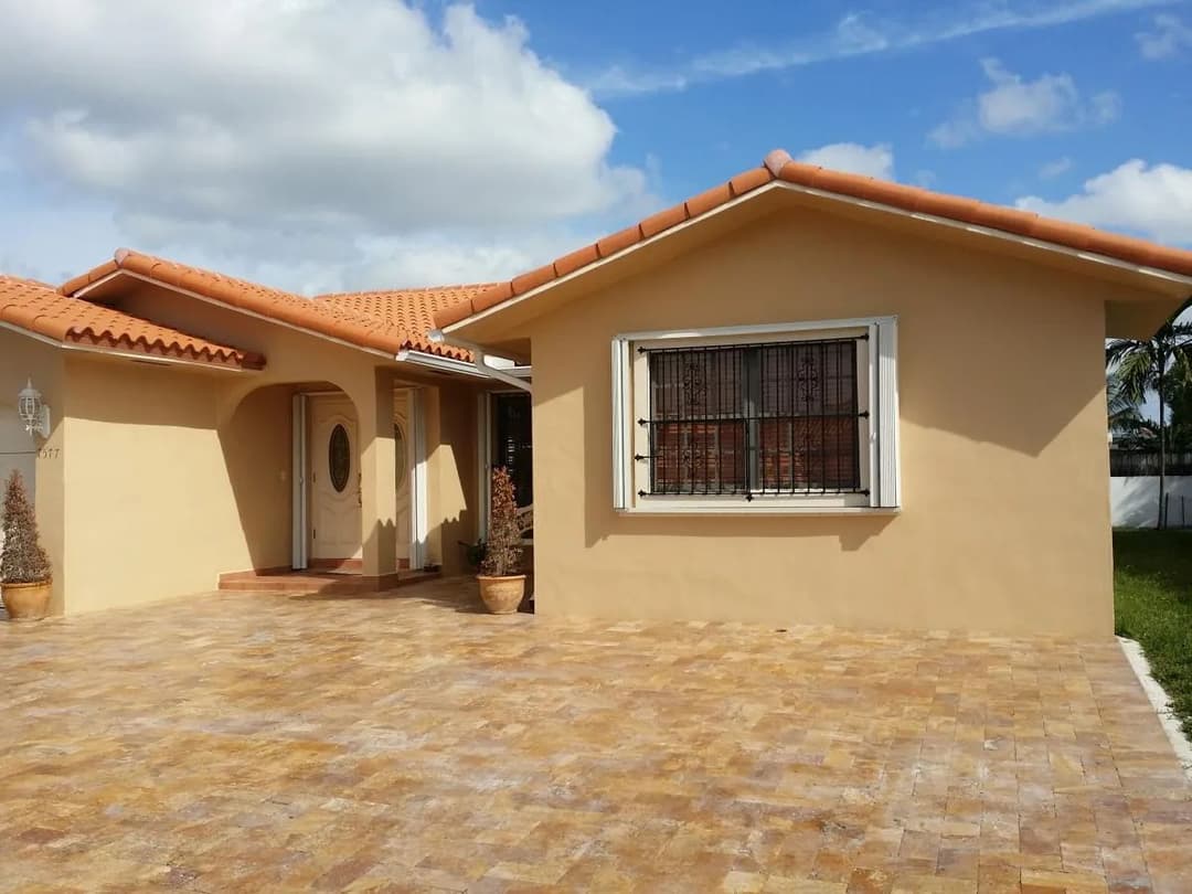 Single-story beige house with red tile roof, decorative windows, and stone patio.