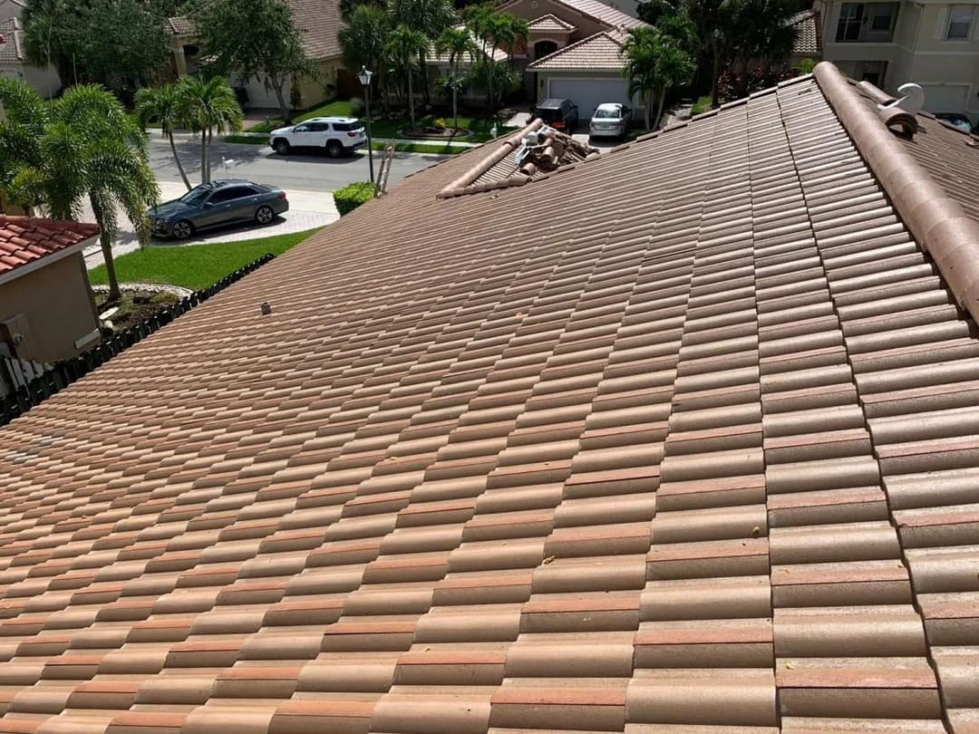 Aerial view of a roof with terracotta tiles, surrounded by green lawns and parked cars.