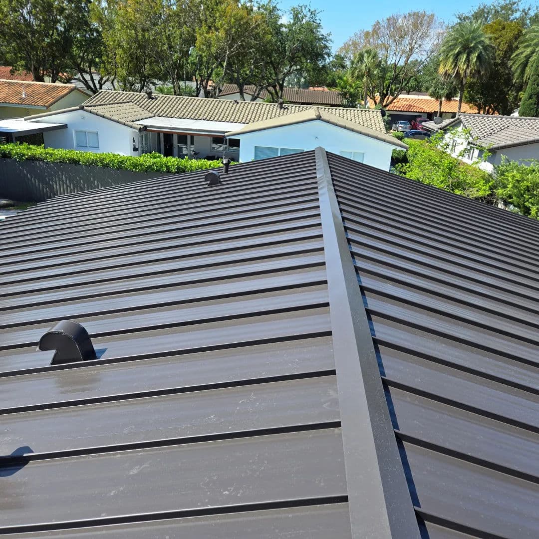 Metal roof installation on a residential home with trees and houses in the background.