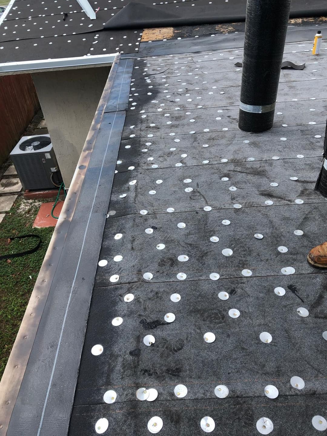 Newly installed roofing membrane with adhesive fasteners on a residential roof.