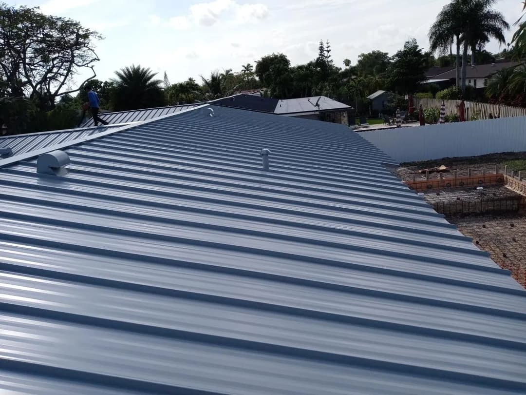 Metal roof installation on residential home with clear blue skies and palm trees in the background.