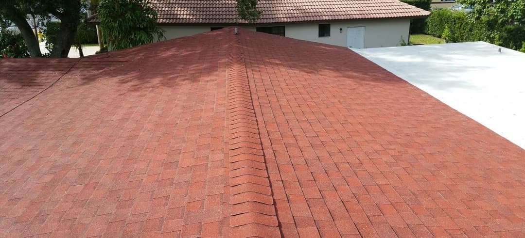 Red asphalt shingle roof with clean lines and a flat roof section in the background.