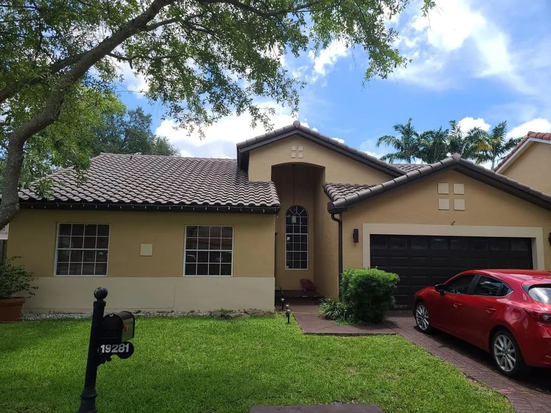 Single-story home with a brown tiled roof, red car parked, and lush green lawn.