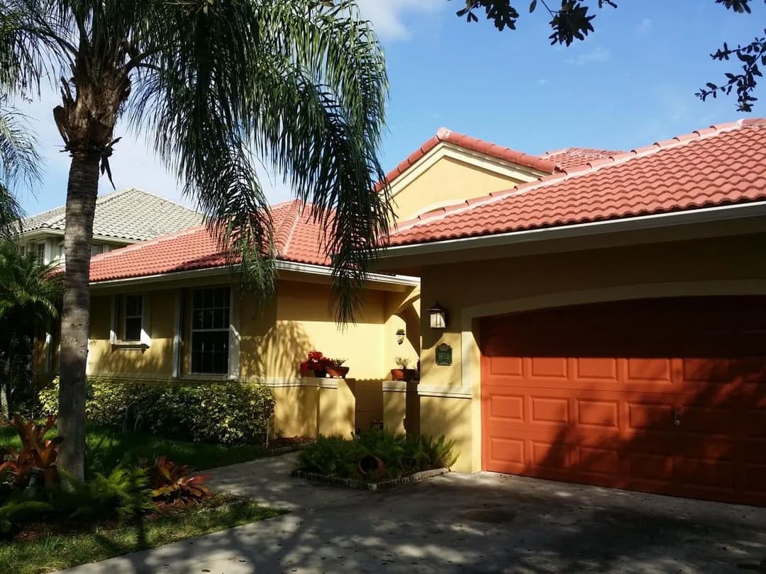Yellow house with red tile roof, palm trees, and a two-car garage in a sunny neighborhood.