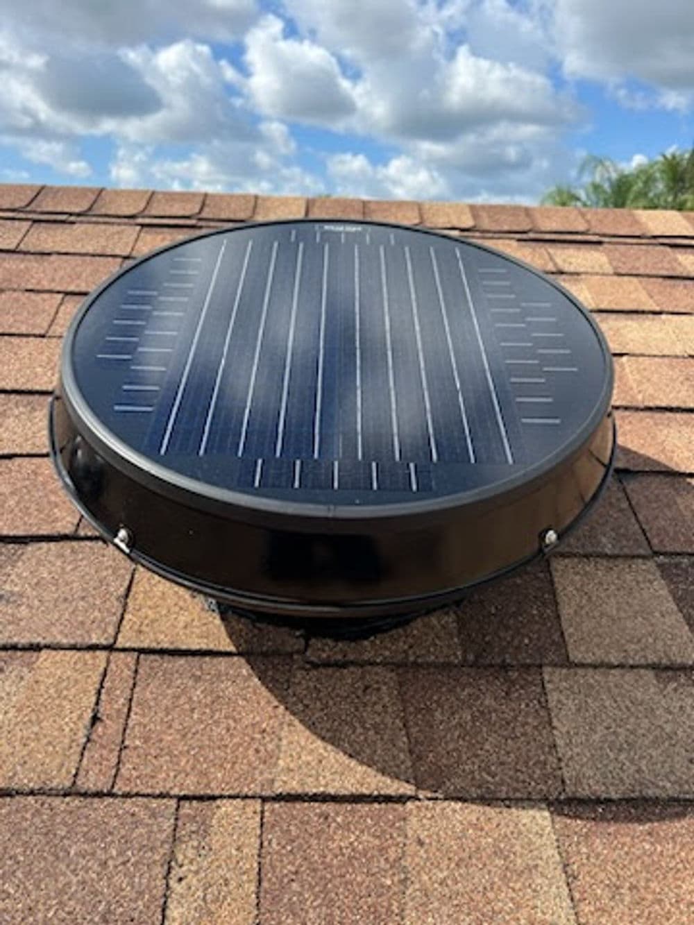 Solar attic fan on a shingle roof under a partly cloudy sky, promoting energy efficiency.
